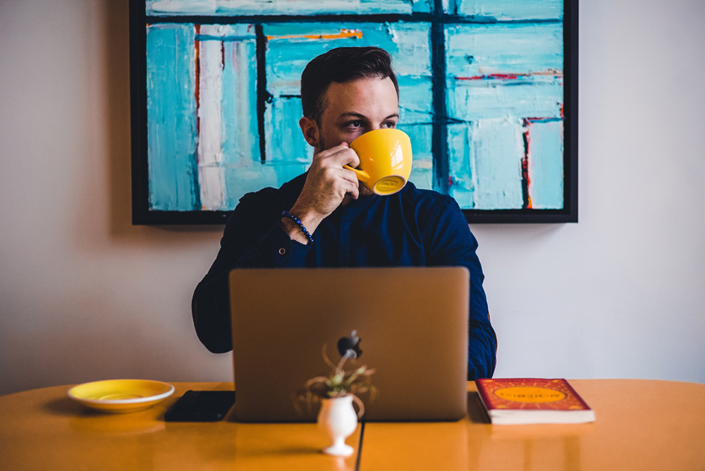 man drinking from mug in front of laptop