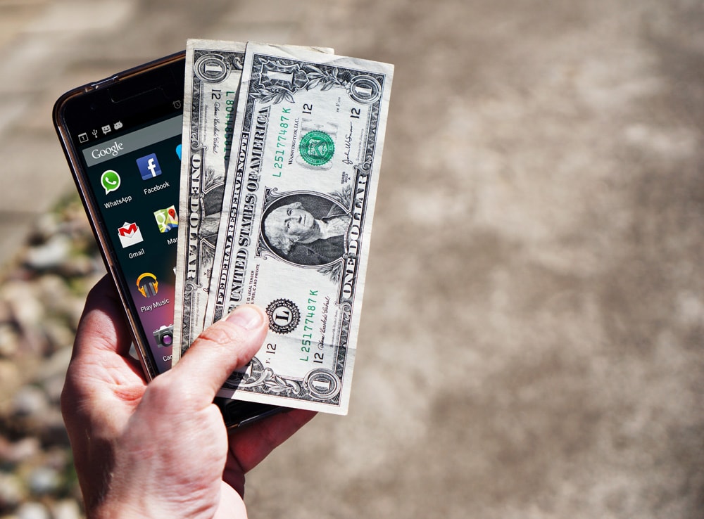 person holding smartphone and dollars