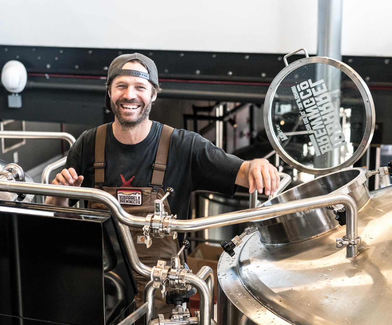 smiling man standing next to brewery equipment