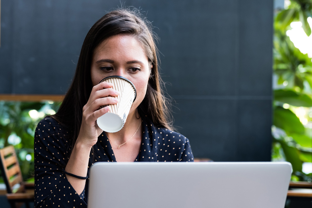 woman sitting drinking coffee looking at laptop computer