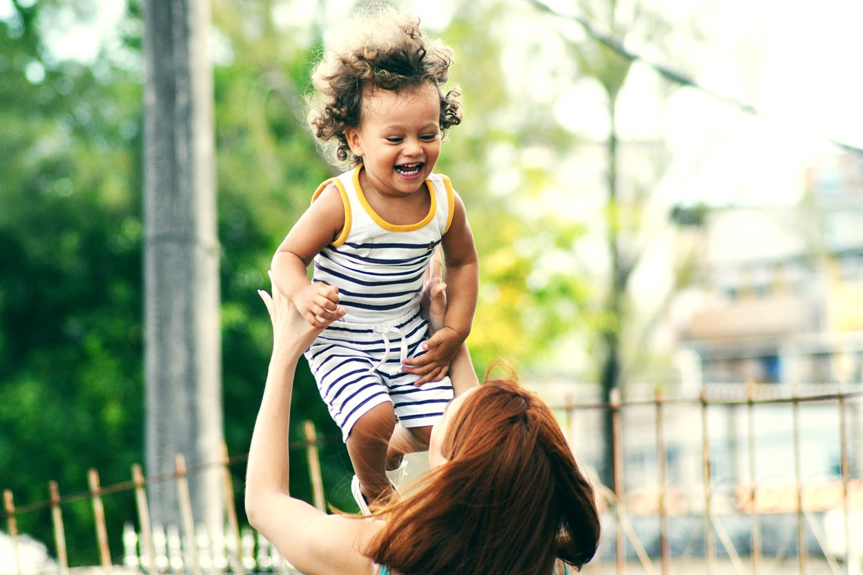 woman lifting and playing with child during daytime